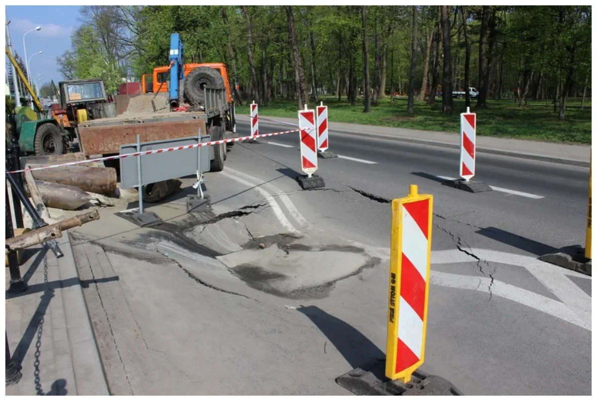 Zdjęcie uszkodzonej nawierzchni ulicy ogrodzonej taśmą i zaporami w biało-czerwone pasy